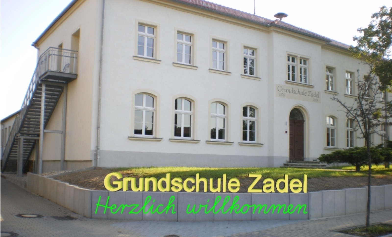 Historisches Gebäude der Grundschule Zadel mit Vorplatz und Bäumen